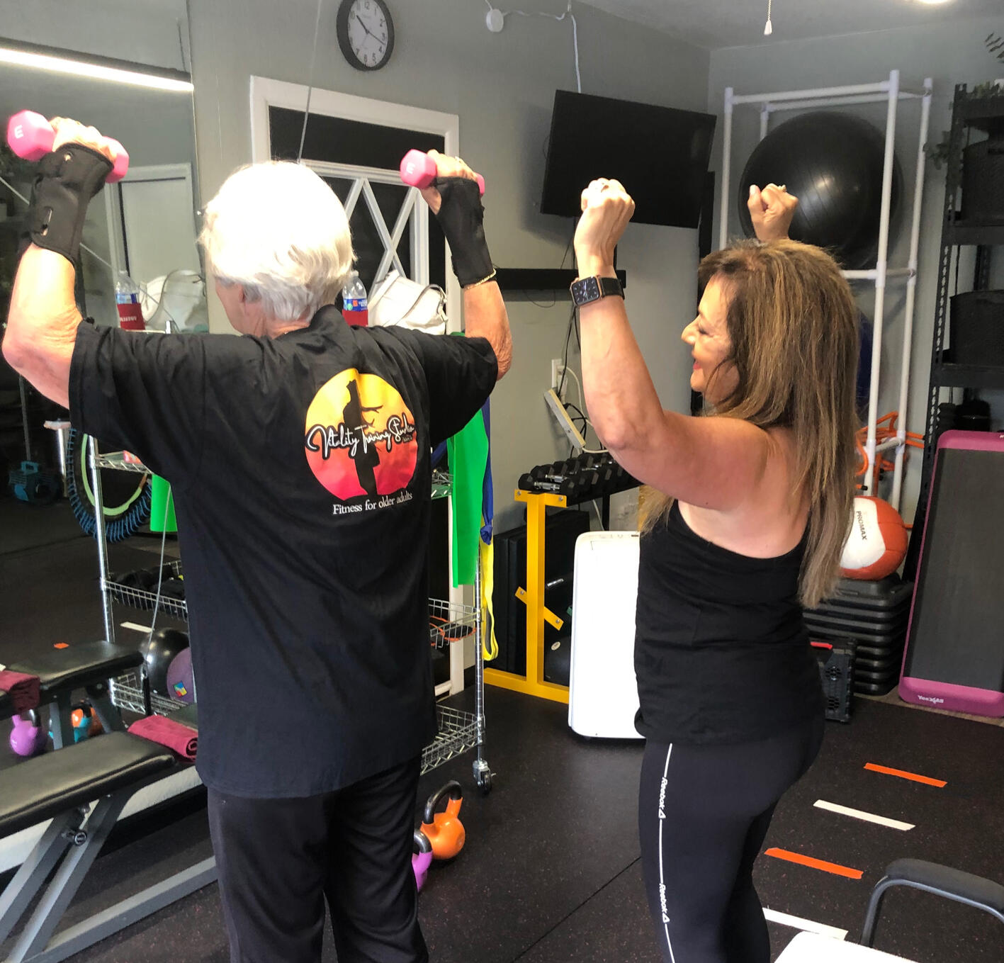 A woman demonstrating a fitness exercise to another woman lifting dumbbells